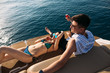 Young caucasian good-looking man and his beautiful girlfriend in bikini sunbathing with cocktails and music on yacht. Happy couple on vacation with beautiful sea views of calm blue water