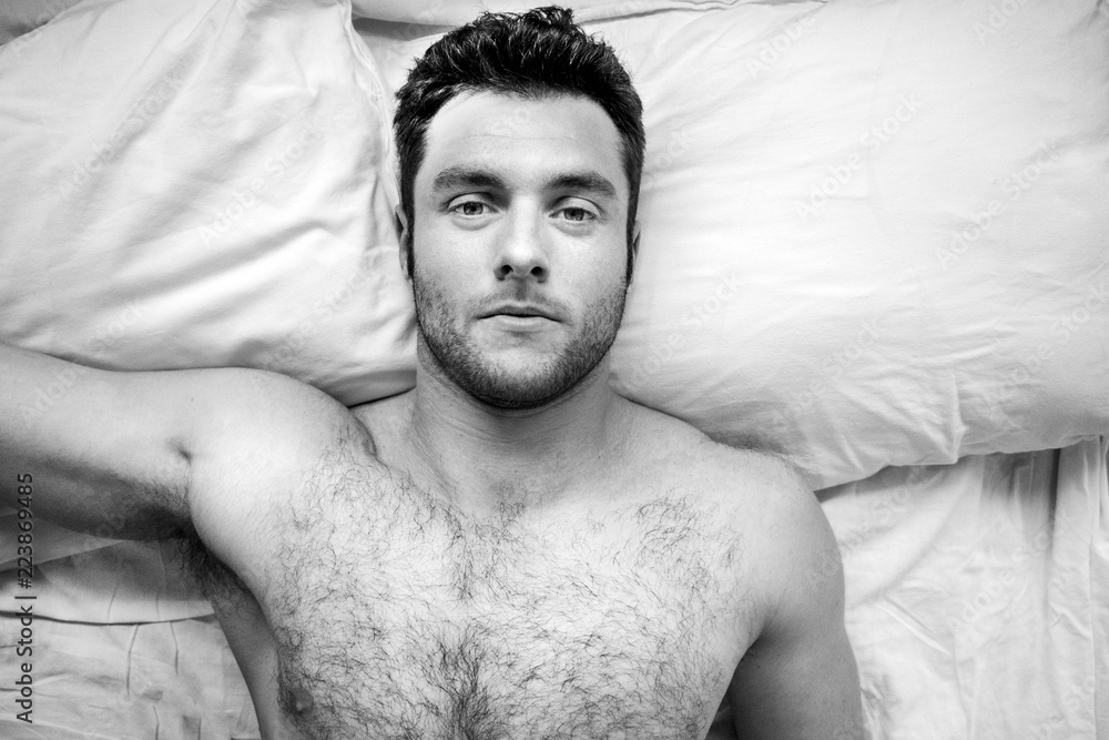 Shirtless sexy hunky man with beard and six pack abs lies naked in bed