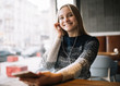 © Oleksii - Beautiful smiling woman listening to music, using headphones and smartphone in loft cafe. Young positive female holding mobile phone, enjoying sound of music