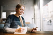 © Oleksii - Beautiful smiling university student studying at modern library, researching information online. Cute caucasian woman sitting in cafe, planning working process. Exam preparation.