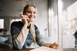© Oleksii - Portrait of young smiling business woman sitting in  modern cafe using mobile phone and writing notes. Skilled freelancer working project at modern office. Successful business