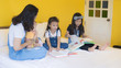 © Sirirat Makprasert - Babysitting playing with three playful kids carrying on the bed; widow young woman and child are enjoying fun time indoor in modern yellow bed room; mother and three daughter; Happy family