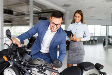 Wall Mural - Saleswoman at the dealership showroom talking with customer and helping him to choose a new motorcycle for himself.