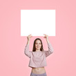 © sementsova321 - Slim beautiful Caucasian woman in casual clothes, holds white blank white card for your advertisement or promotional content, isolated over pink studio background. Free space. Vertical shot.