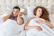 Stressful man suffers from insomnia, keeps pillow on head while hears wifes snoring during night, sleep together in one bed. Curly woman has problems with health, interrupts man to sleep well