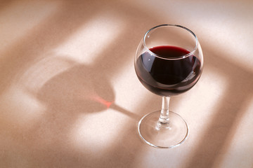 Red wine glass on the table with window shadow