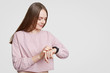 © sementsova321 - Attractive woman looks at smartwatch, checks calories or pulse, wears casual oversized sweater, has dark staight hair, isolated on white background with free space. Modern technologies and innovations