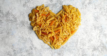 Top view of golden shape of heart made of uncooked pasta mix on marble white table