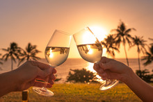 Couple Cheers With Wine Glasses In A Beautiful Sunset Beach Setting. 
