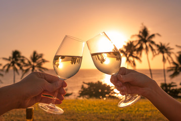 Couple cheers with wine glasses in a beautiful sunset beach setting. 
