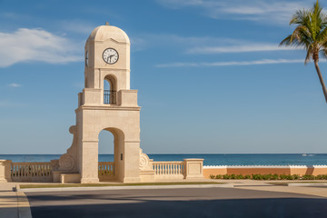 A tall clock tower timepiece stands at the of the road overlooking the ocean.