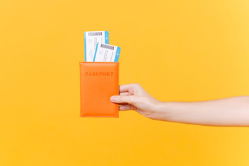 Close up tourist female horizontal hold in hand two tickets for plane with orange passport, boarding pass, isolated on yellow background. Copy space advertising area. Air flight journey travel concept