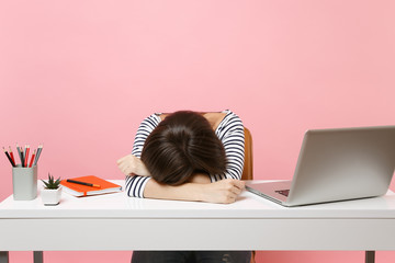 Young Disappointed Tired woman laid her head down on the table sit, work at white desk with contemporary pc laptop isolated on pastel pink background. Achievement business career concept. Copy space.