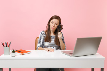 Wall Mural - Young Curious woman scrutinizing looking through magnifying glass on pc laptop while sit work on project at office isolated on pastel pink background. Achievement business career concept. Copy space.