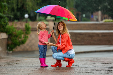 Wall Mural - Happy mother and daughter with bright umbrella under rain outdoors