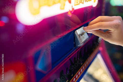 Fotografija Child hand inserting a coin into the amusement park arcade machine