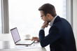 © fizkes - Thoughtful male CEO looking at laptop screen making decision or writing business email, serious businessman thinking about contract or deal terms, man busy analyzing statistics preparing report