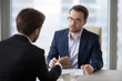 Focused male business partners negotiate at office table discussing statistics, male managers talk about sales and contract terms, businessmen consider deal closing, speak about success strategies