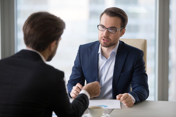 Sticker - Focused male business partners negotiate at office table discussing statistics, male managers talk about sales and contract terms, businessmen consider deal closing, speak about success strategies