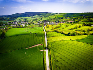 Wall Mural - Aerial view looking down on a rural road in the UK countryside with a car racing along it. On a bright sunny day, farmland and crops can be seen either side of the road