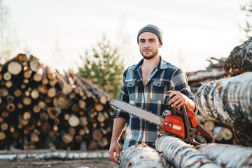 Wall Mural - Bearded strong lumberjack wearing plaid shirt hold in hand chainsaw for work on sawmill