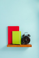 Poster - notepad and alarm clock on shelf at wall background