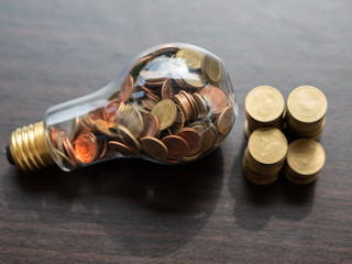 Wall Mural - energy saving. stacks of coins in light bulb on wooden floor background. saving, accounting and fina