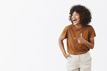 Cannot Hide True Happiness. Portrait Of Joyful Charming Carefree African American Woman With Curly Hairstyle Looking And Pointing Left With Finger Gun Laughing From Happiness And Good Mood