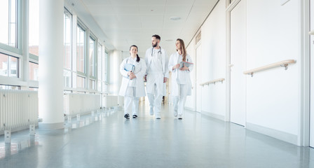 Poster - Doctors, two women and a man, in hospital walking down the corridor