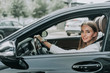 © Yakobchuk Olena - Portrait of smiling girl keeping steering wheel while driving automobile. She looking at camera during trip at job