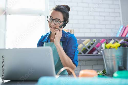 Fotografía Waist up portrait of modern young businesswoman speaking by phone and using lapt