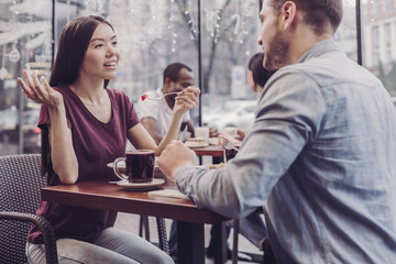 Wall Mural - Emotional talk. Charming international girl keeping smile on her face and eating salad with pleasure