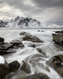 Fototapeta Łazienka - Coastal landscape in winter with water movement between big stones, in the background a mountain range with snow, high contrast sky - Location: Norway, Lofoten