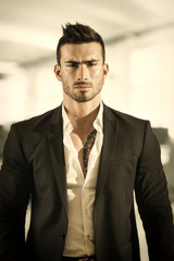 Handsome young male worker in office building, standing, looking at camera wearing white shirt open on neck and business suit jacket