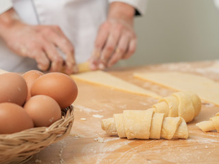 Chef hands are rolling a croissant from dough on wooden board. black background.