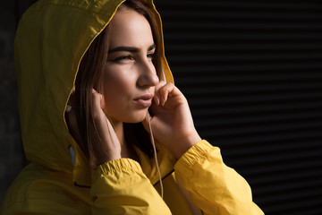 Serious woman under yellow hood with earbuds listening a music