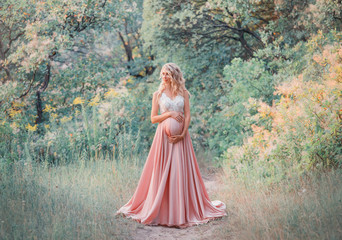 young sweet pregnant girl with light curly hair hugs and holds her tummy, standing in a fairy forest in cold shades. dresses a long elegant satin silk pink dress with a lace top. art processing photo