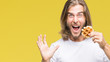 Young handsome man with long hair over isolated background eating waffle very happy and excited, winner expression celebrating victory screaming with big smile and raised hands