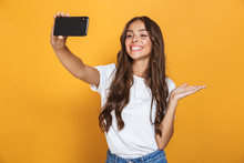 Portrait Of Positive Woman 20s With Long Hair Laughing While Taking Selfie Photo On Smartphone, Isolated Over Yellow Background