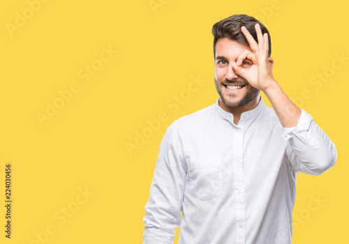 Fotografia Young handsome man over isolated background doing ok gesture with hand smiling, eye looking through fingers with happy face