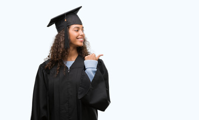 Wall Mural - Young hispanic woman wearing graduation uniform pointing and showing with thumb up to the side with happy face smiling