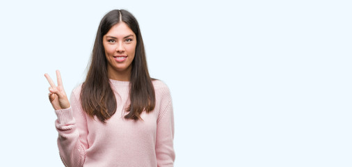 Young beautiful hispanic woman wearing a sweater showing and pointing up with fingers number two while smiling confident and happy.