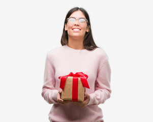 Poster - Young hispanic woman holding a gift with a happy face standing and smiling with a confident smile showing teeth