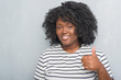© Krakenimages.com - Young african american plus size woman over grey grunge wall doing happy thumbs up gesture with hand. Approving expression looking at the camera with showing success.