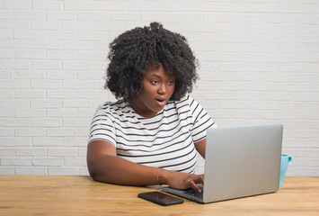 Poster - Young african american woman sitting on the table using computer laptop scared in shock with a surprise face, afraid and excited with fear expression