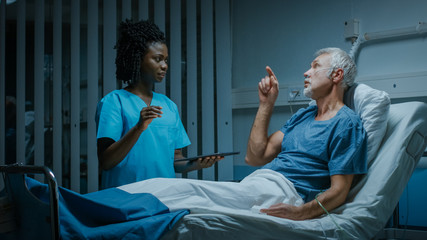 Wall Mural - In the Hospital, Senior Patient Lying in the Bed Nurse Holding Tablet Computer Shows Augmented Reality Information, They Both Make Gestures and Talk. In the Technologically Advanced Hospital Ward.