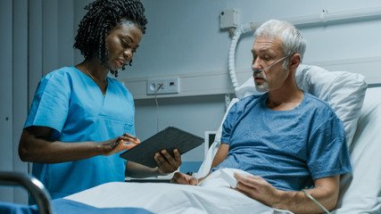 Wall Mural - In the Hospital, Senior Patient Lying in the Bed Talking to a Nurse who is Holding Tablet Computer Showing Him Information. In the Technologically Advanced Hospital Ward.