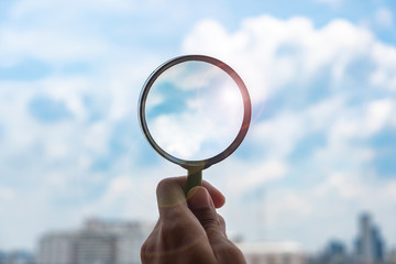 hands holding glass magnify against blue sky background. Business Explore, Searching, Discovery and Vision concepts