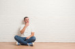 © Krakenimages.com - Young caucasian man sitting on the floor over white brick wall looking confident at the camera with smile with crossed arms and hand raised on chin. Thinking positive.