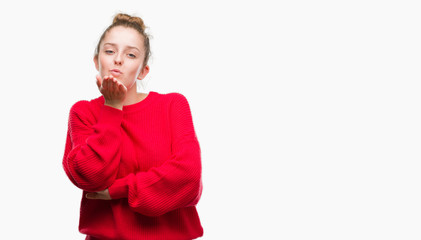 Wall Mural - Young blonde woman wearing bun and red sweater looking at the camera blowing a kiss with hand on air being lovely and sexy. Love expression.